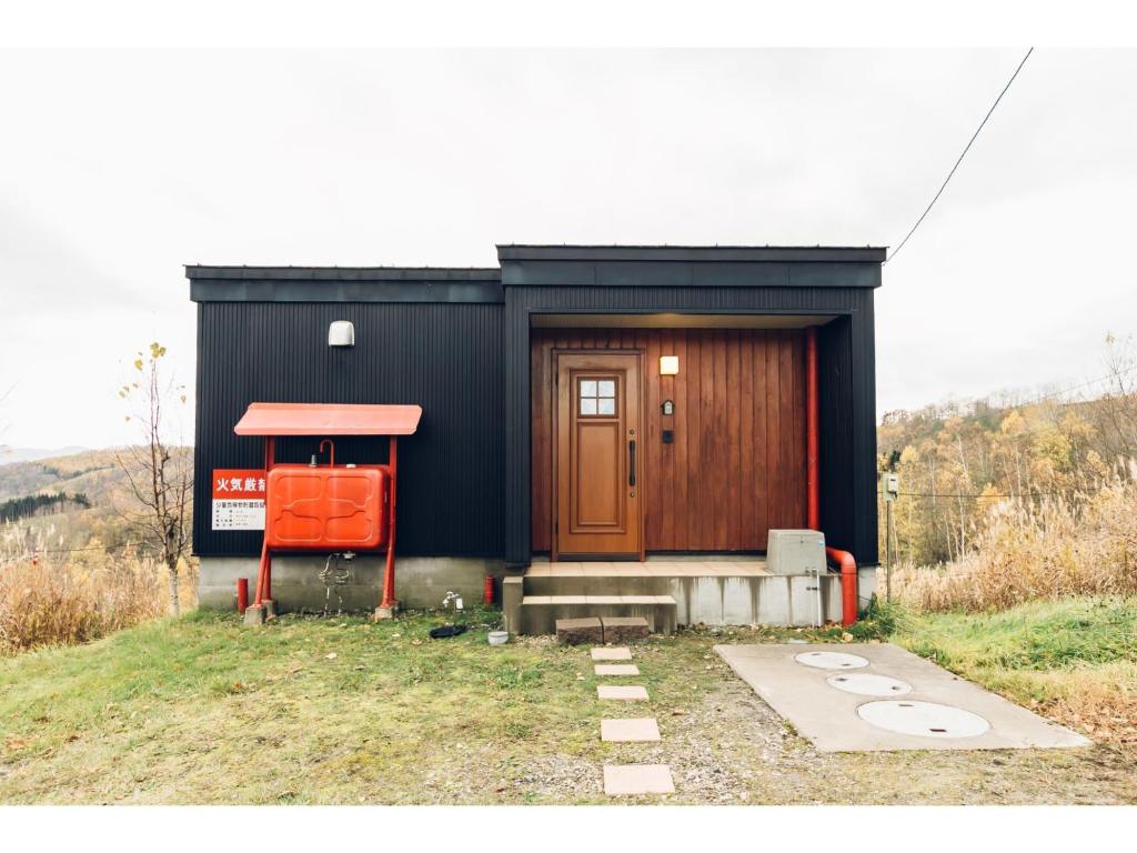 una pequeña casa negra con una puerta roja en una colina en LAKE view PRIVATE log house en Lake Toya