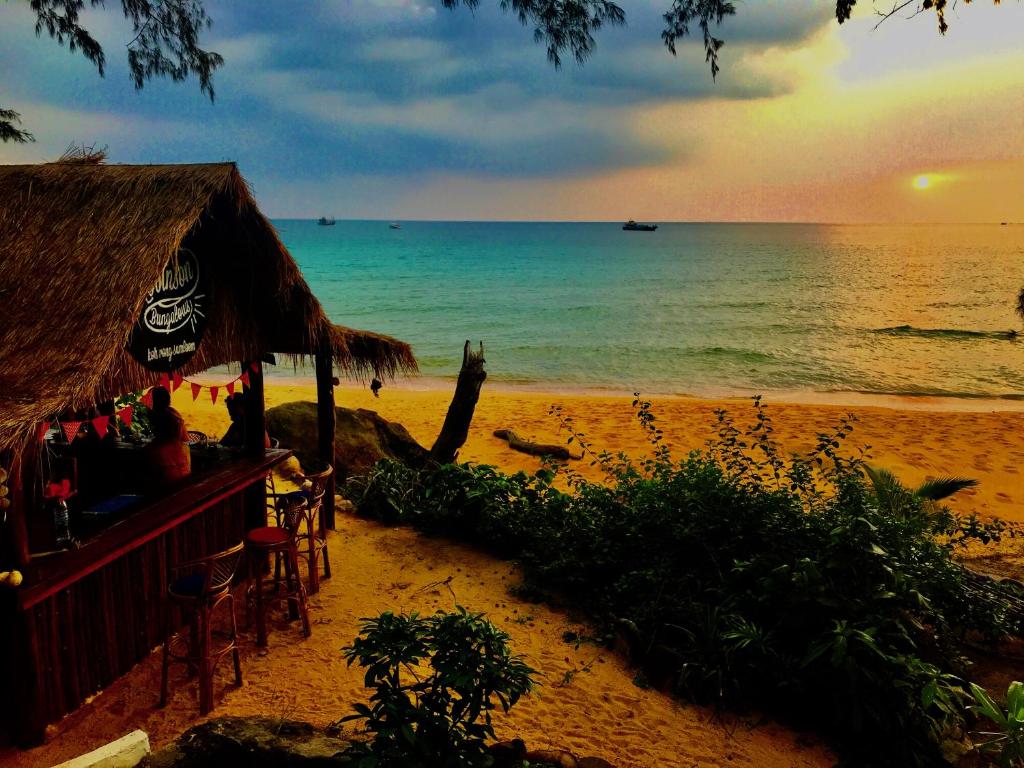 a beach with a bar and the ocean at sunset at Robinson Bungalows in Koh Rong Sanloem