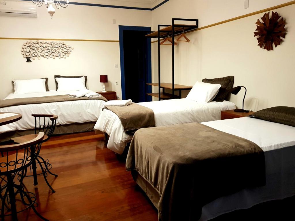 um quarto de hotel com três camas e uma mesa e cadeiras em Suíte Marília de Dirceu em Ouro Preto