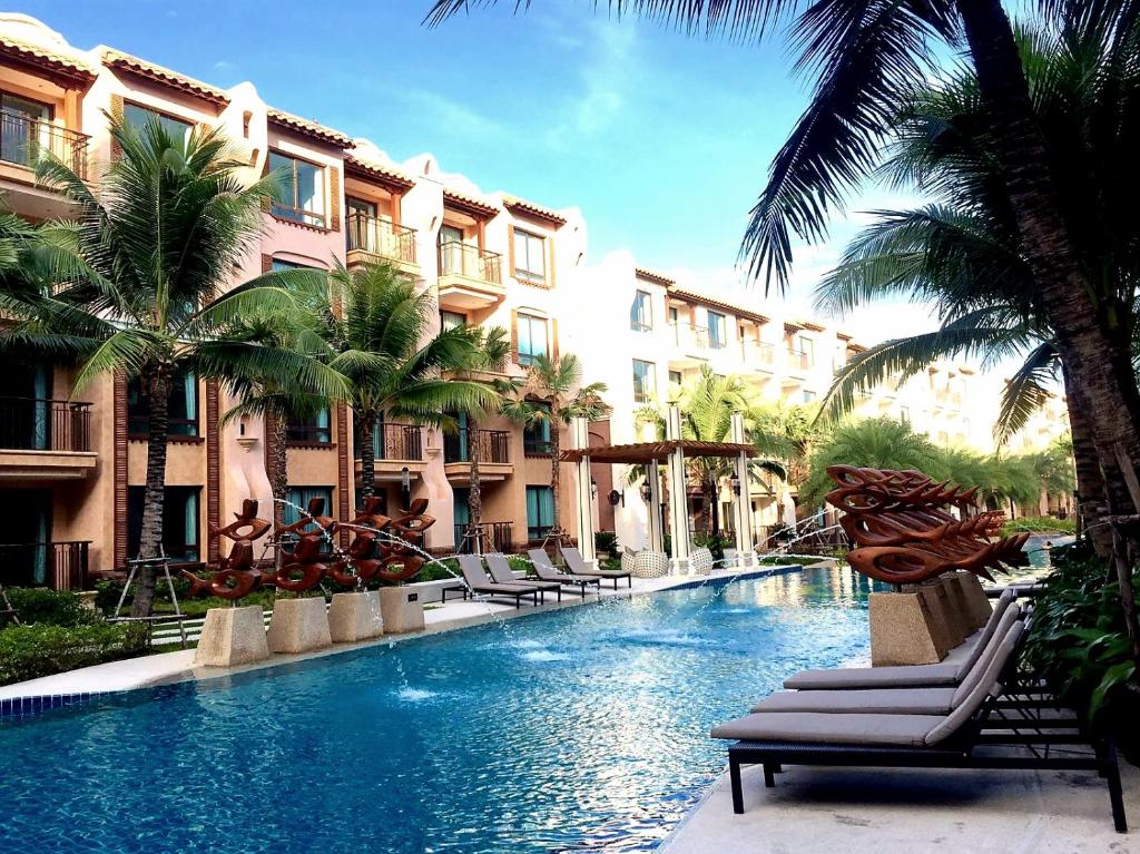 a swimming pool with chairs and palm trees next to buildings at Peaceful Pool-access room - Q seaside Hua Hin in Phetchaburi