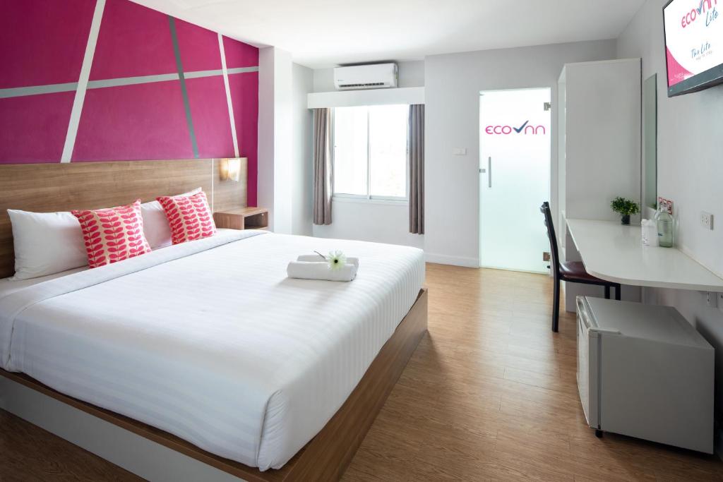 a bedroom with a large white bed and a pink wall at Eco Inn Lite Nakhon Si Thammarat in Nakhon Si Thammarat