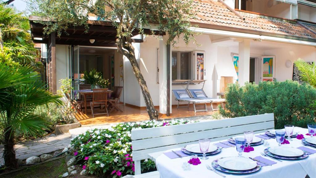 - une table blanche avec des assiettes et des verres à vin dans un jardin dans l'établissement Villa Scultura Seaview, à Lignano Sabbiadoro