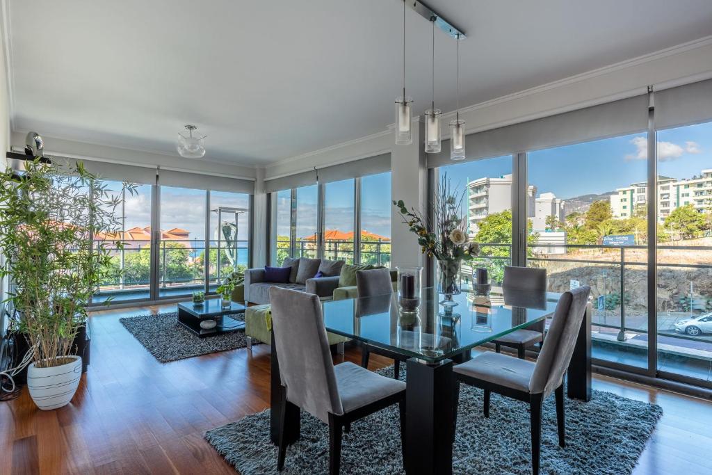 uma sala de jantar com uma mesa e cadeiras de vidro e janelas grandes em Monumental Residence apartment with pool by HR Madeira no Funchal