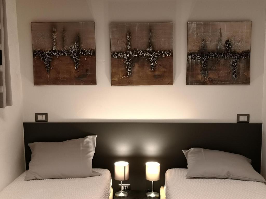 dwa łóżka w pokoju z trzema zdjęciami na ścianie w obiekcie DOMUSCUNEO Barra di Ferro 3 bianco w mieście Cuneo