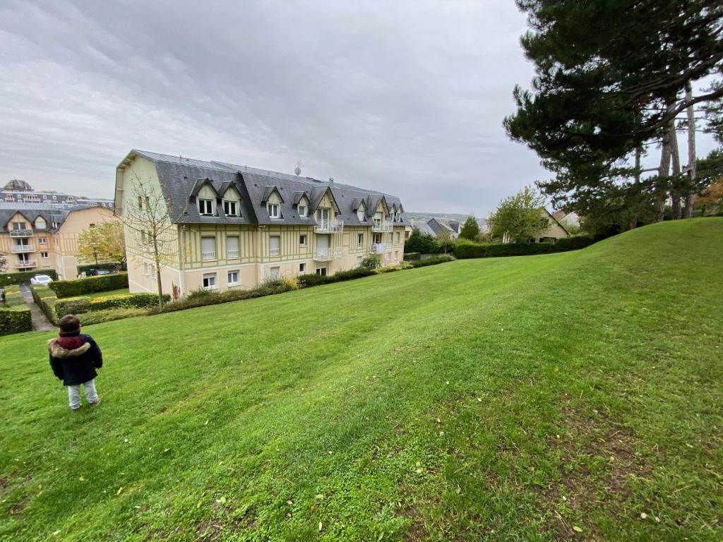 Ein kleiner Junge steht auf einem Feld vor einem großen Haus in der Unterkunft Vallon 3 pièces avec balcon in Trouville-sur-Mer