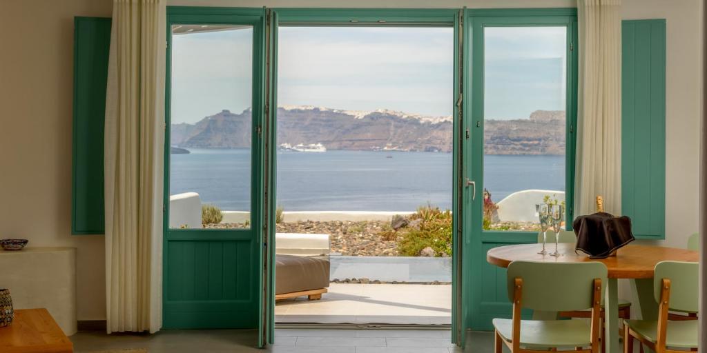 a room with green doors and a table with a view of the ocean at Neptune Luxury Suites in Akrotiri