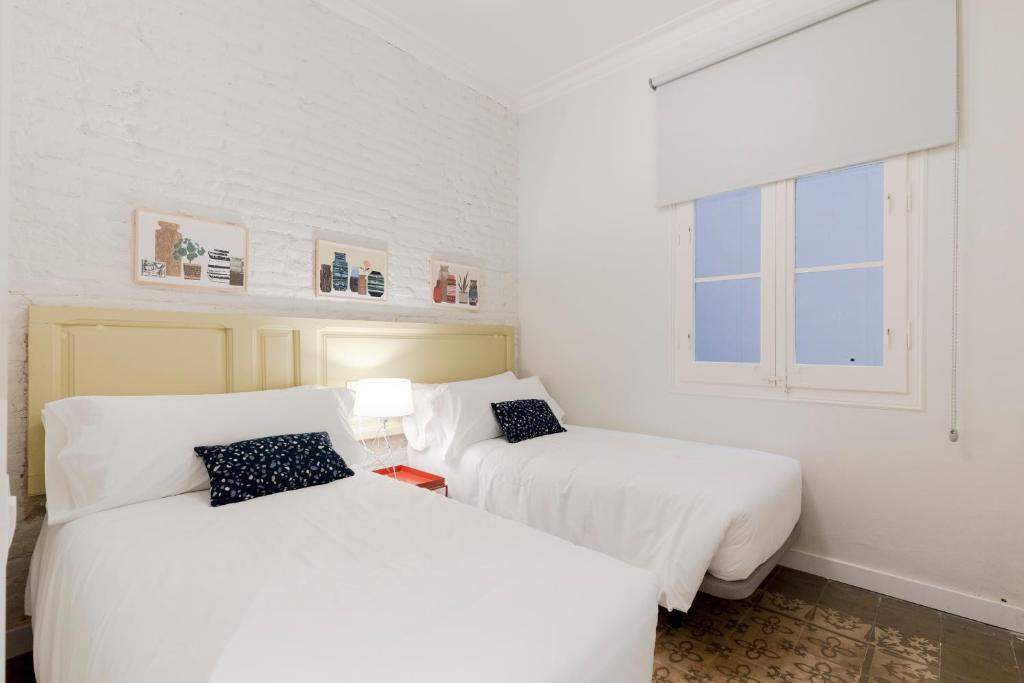 Aspasios Gracia Apartments في برشلونة: سريرين في غرفة بجدران بيضاء ونوافذ