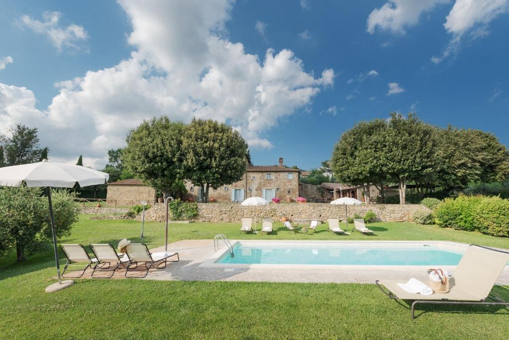 a pool with chairs and an umbrella in a yard at Villa Torre degli Elci in Cortona
