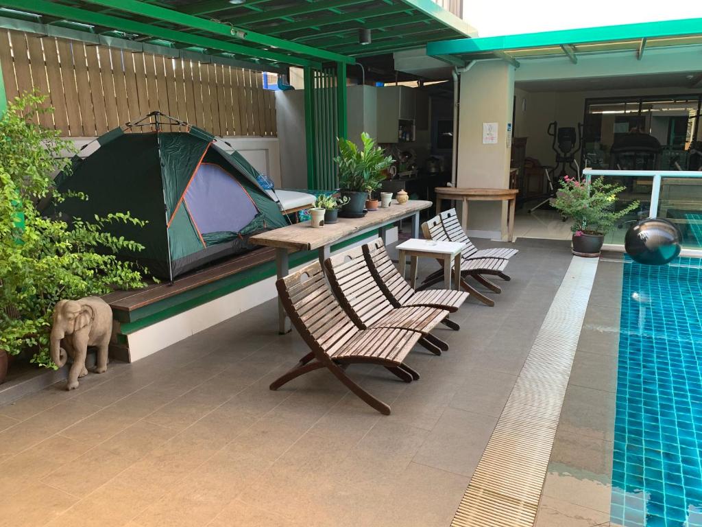 A poolside terrace with wooden loungers, tables, potted plants, and a tented seating area.