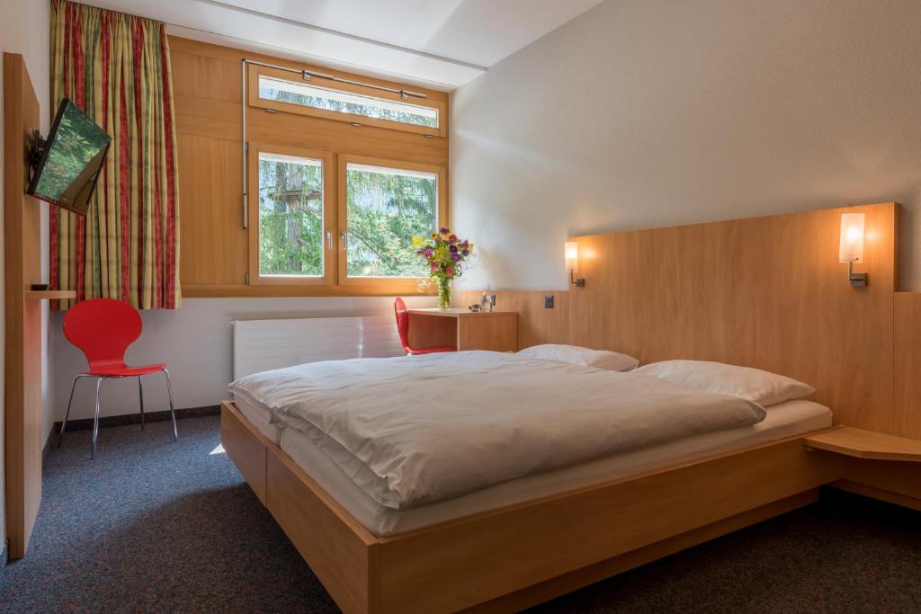 ein Schlafzimmer mit einem großen Bett und einem roten Stuhl in der Unterkunft Sport Resort Fiesch, Garni Aletsch in Fiesch