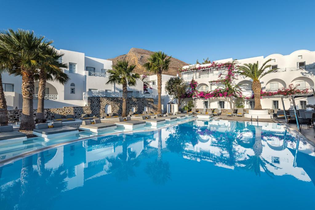 une grande piscine avec des palmiers et des bâtiments dans l'établissement Santorini Kastelli Resort, à Kamari