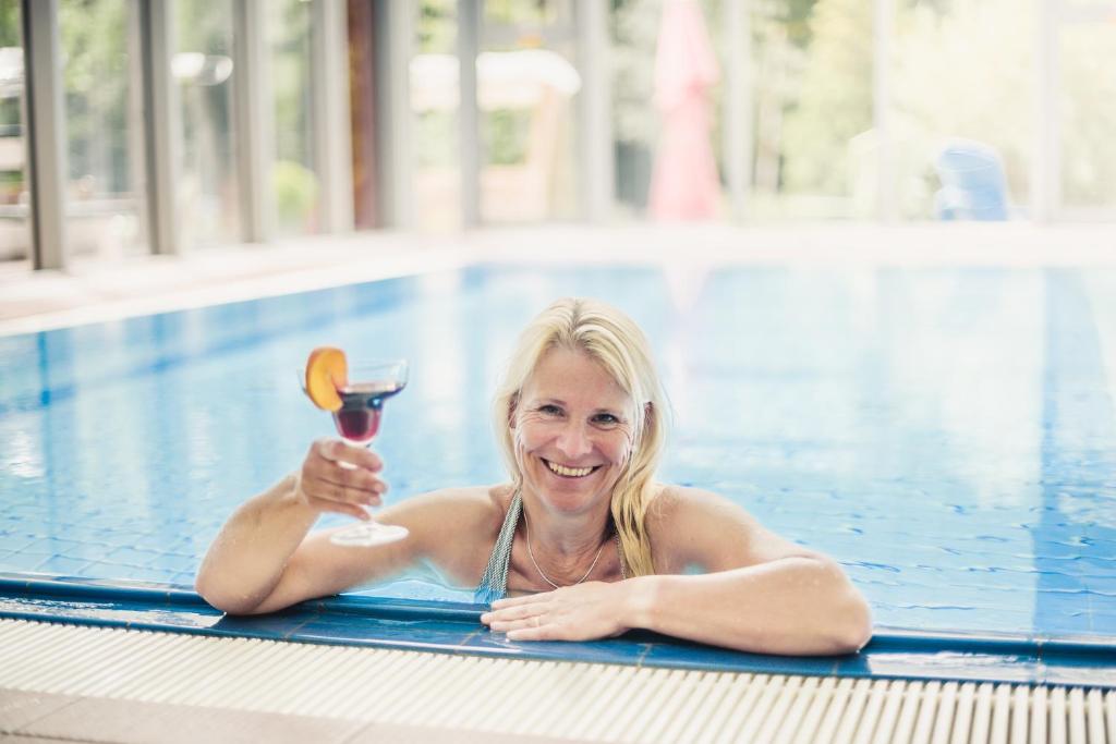 Eine Frau, die in einem Schwimmbad liegt und ein Glas Wein hält. in der Unterkunft Hotel Asgard in Zinnowitz