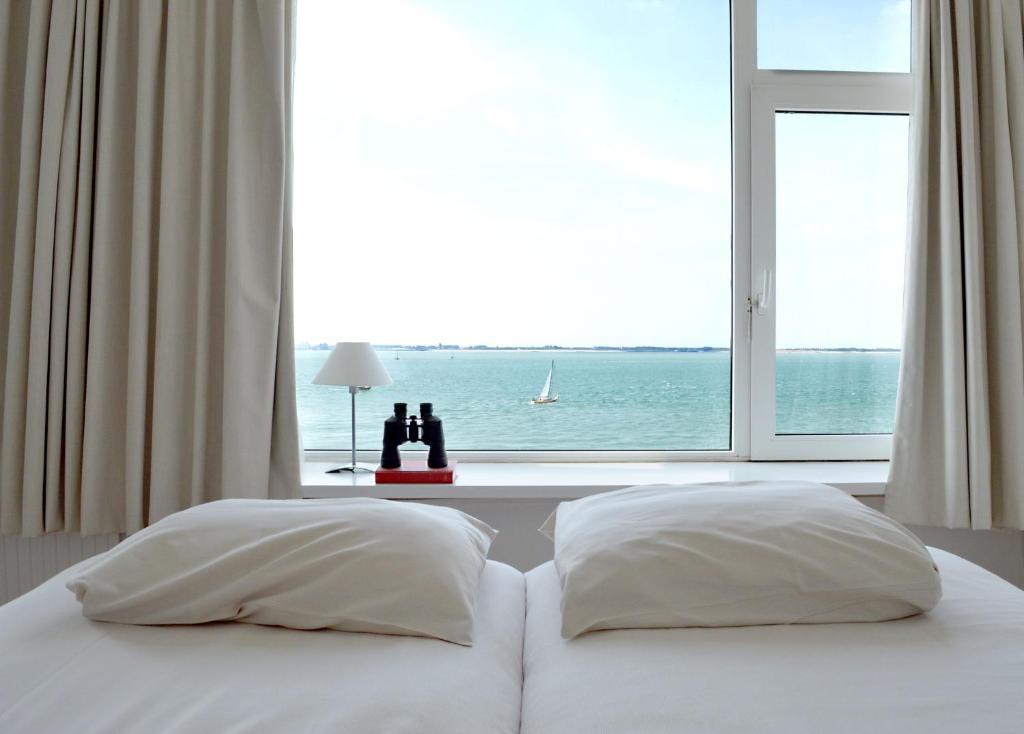 a bed with two pillows in front of a window at Belgische Loodsensociëteit in Vlissingen