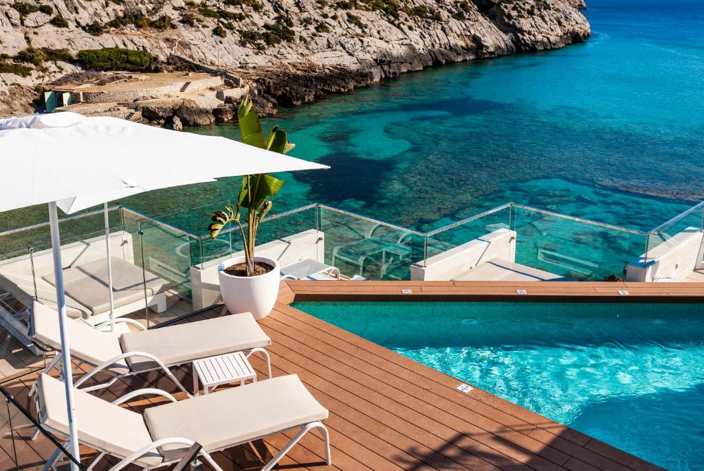 a pool with chairs and an umbrella next to the water at Globales Don Pedro - Adults Only in Cala de Sant Vicenc