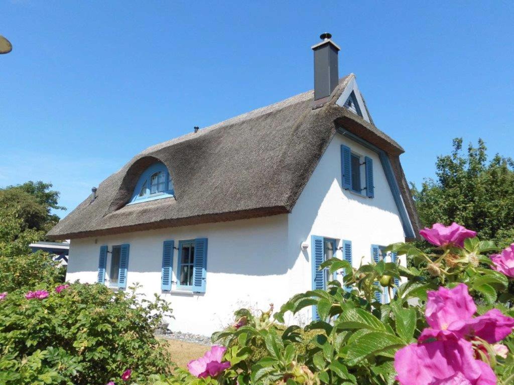 a white house with a thatched roof with pink flowers at Reetdachhaus Kranich in Mursewiek