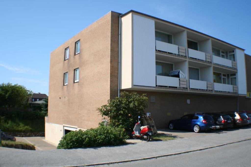 ein Backsteingebäude mit Autos auf einem Parkplatz in der Unterkunft App. Bölting in Wenningstedt-Braderup