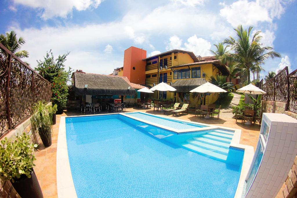 a swimming pool in front of a building with umbrellas at Pousada do Galo in Porto De Galinhas