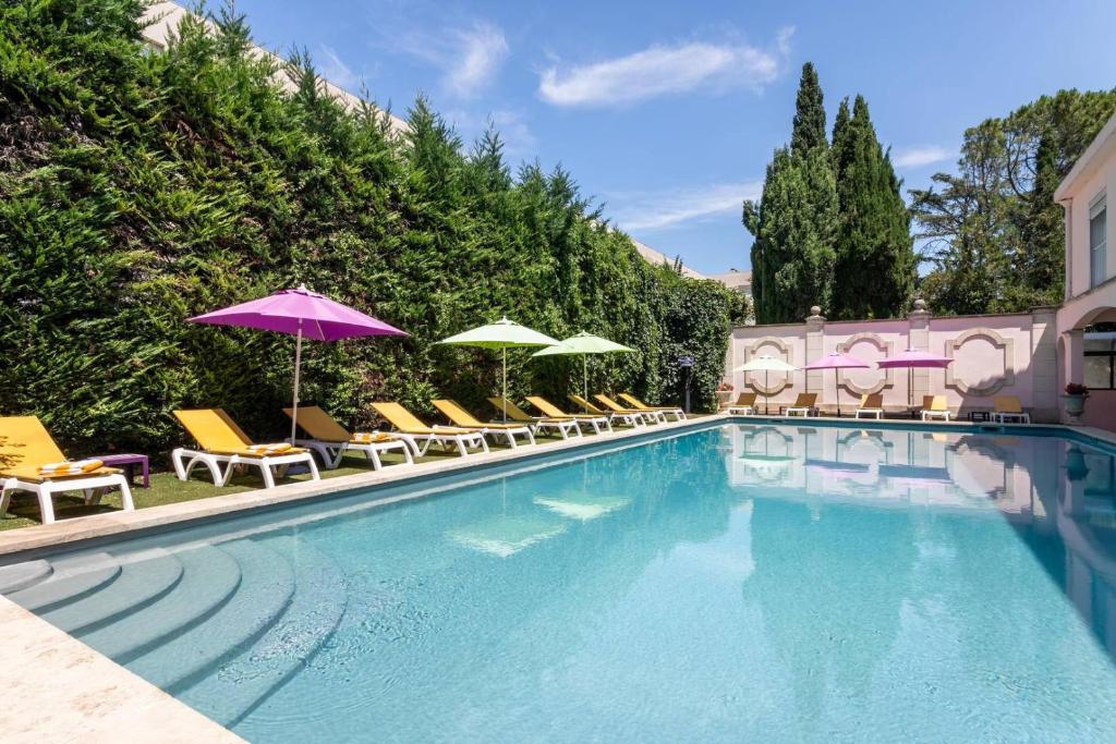 a swimming pool with chairs and umbrellas next to a building at Hôtel Mireille in Arles