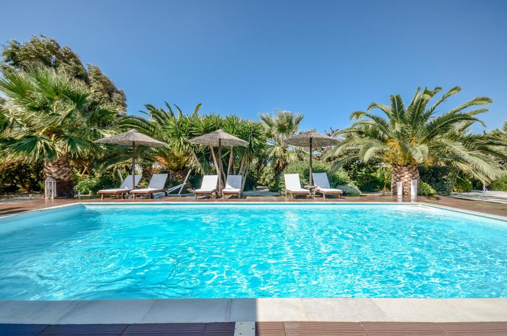 a swimming pool with chairs and palm trees at Valena Mare Suites & Apartments in Plaka