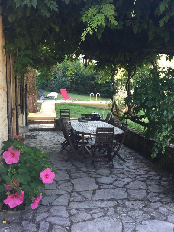 une terrasse avec une table, des chaises et des fleurs roses dans l'établissement Maison en Périgord à 5 mn à pieds du centre Sarlat, à Sarlat-la-Canéda