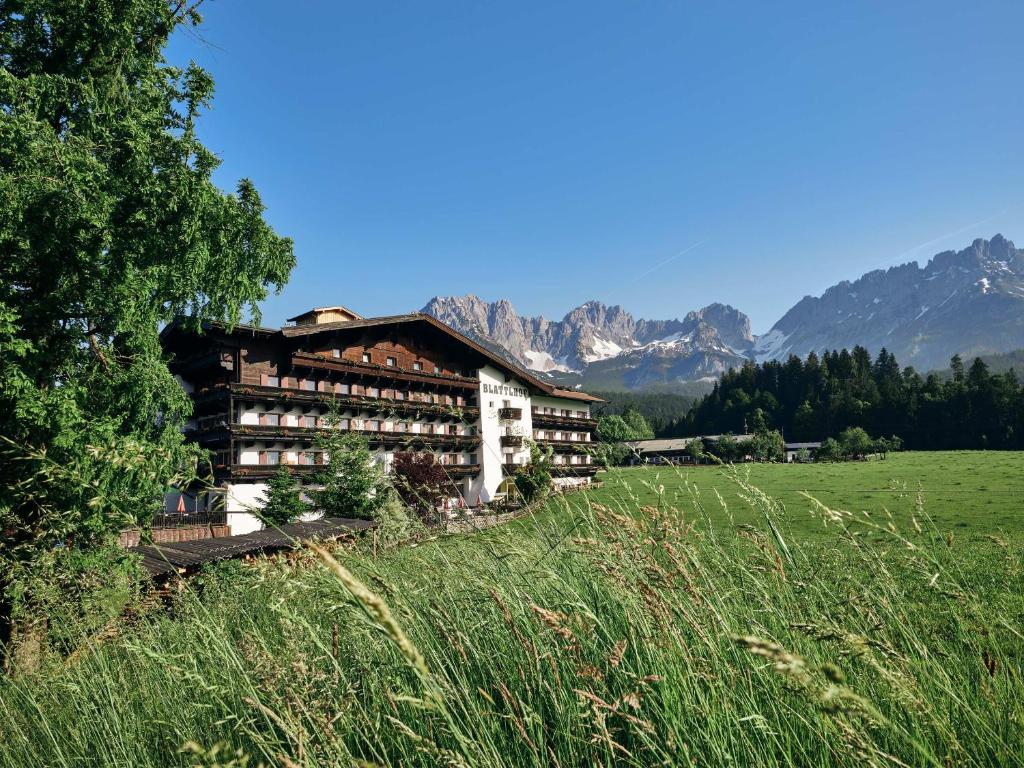 a building in a field with mountains in the background at Hotel Blattlhof in Going am Wilden Kaiser