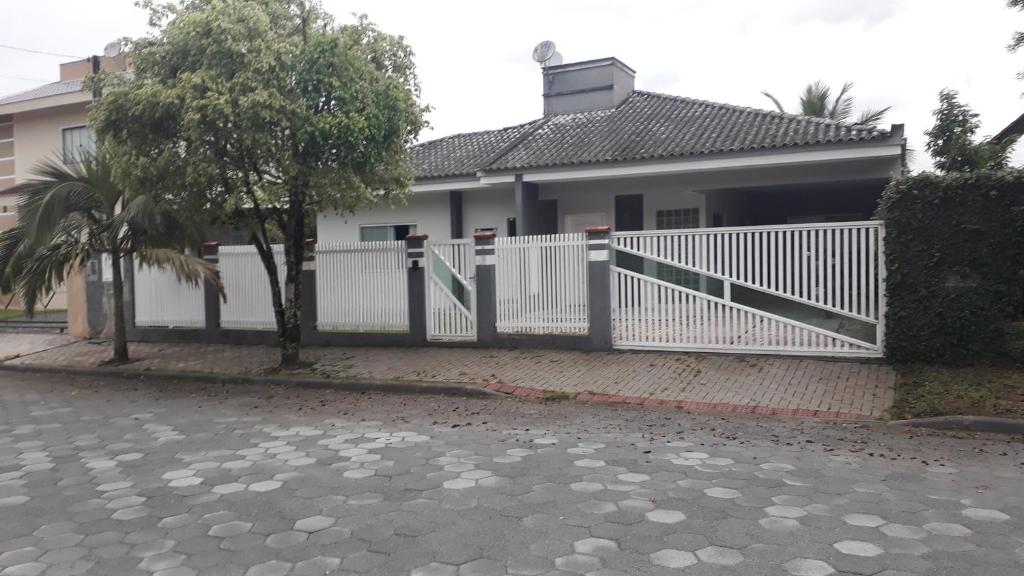 uma cerca branca em frente a uma casa em QUARTOS ACONCHEGANTES.. em Jaraguá do Sul