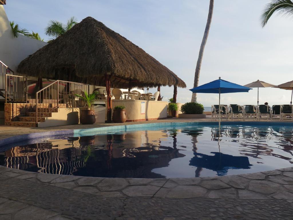 una piscina con sombrilla de paja y un complejo en Suites Atlas - Ocean Front en Bucerías