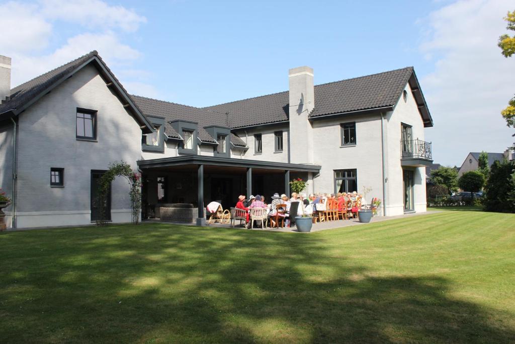 a large white house with people sitting on a lawn at Bed and breakfast Mooi Achel in Achel