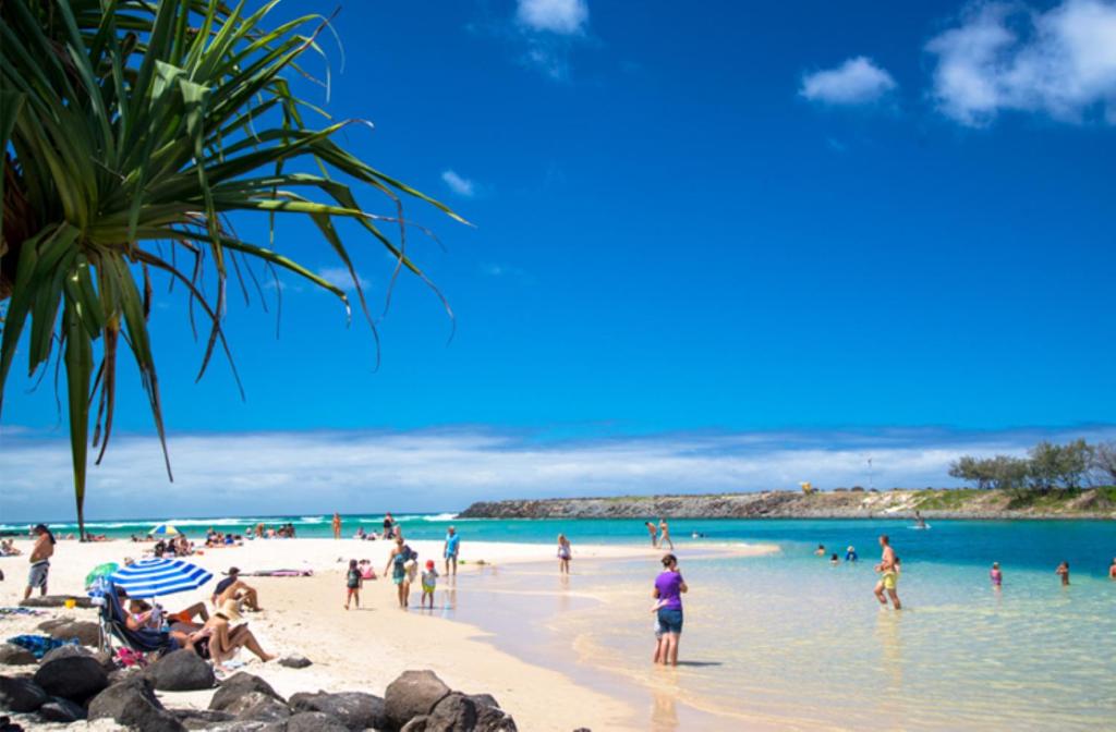 um grupo de pessoas em uma praia no oceano em Sea Mist Palms em Gold Coast