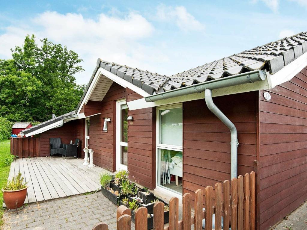 uma casa vermelha com um deque de madeira em 8 person holiday home in Juelsminde em Sønderby