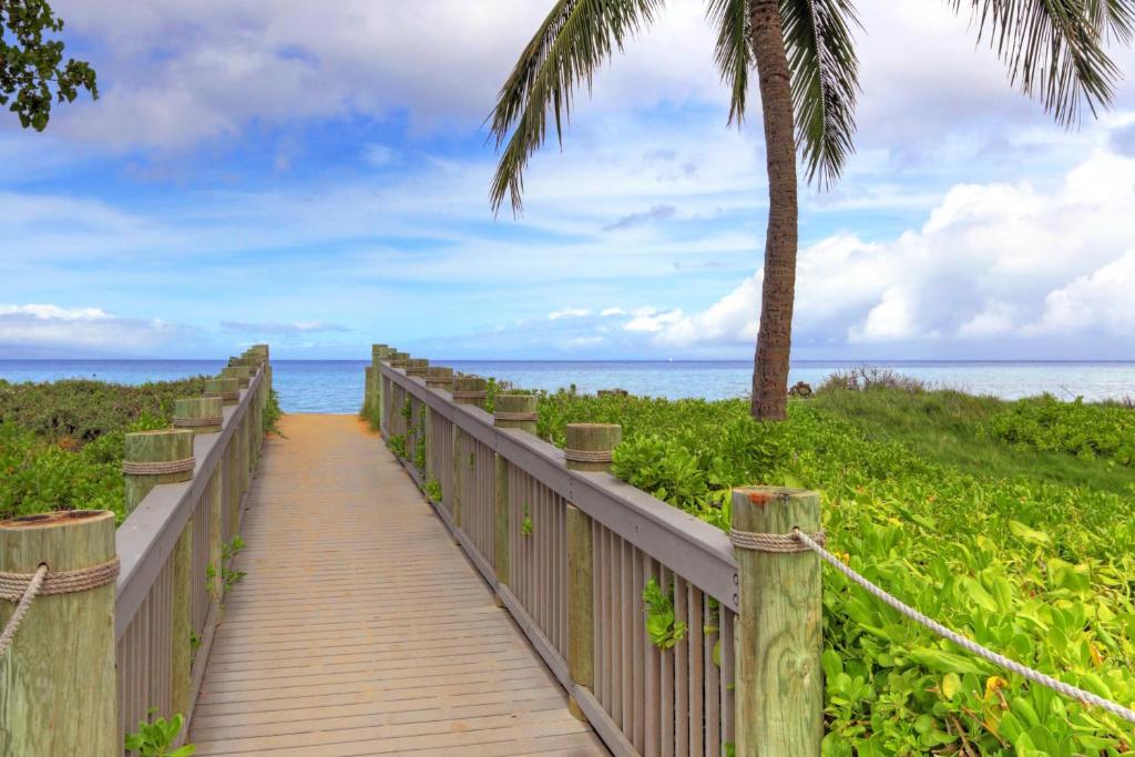 a wooden boardwalk to the beach with a palm tree at Honua Kai - Konea 310 in Kahana