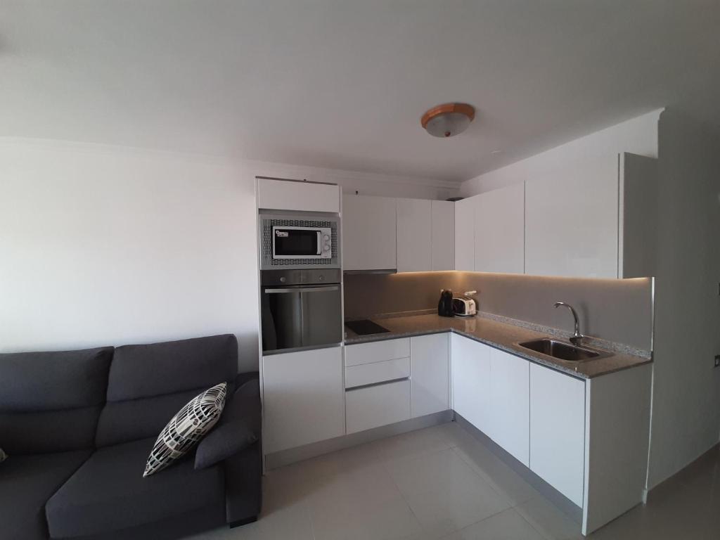 a kitchen with white cabinets and a couch in it at Apartamento Playa in Playa del Ingles