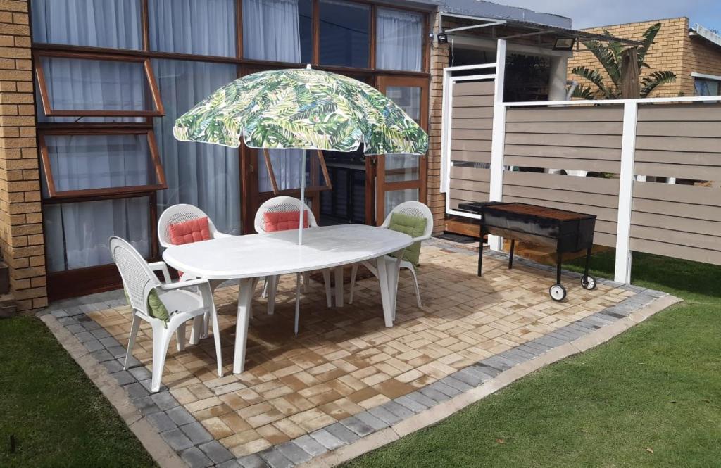 een witte tafel en stoelen met een parasol en een piano bij King Protea Self Catering Flat in Mosselbaai