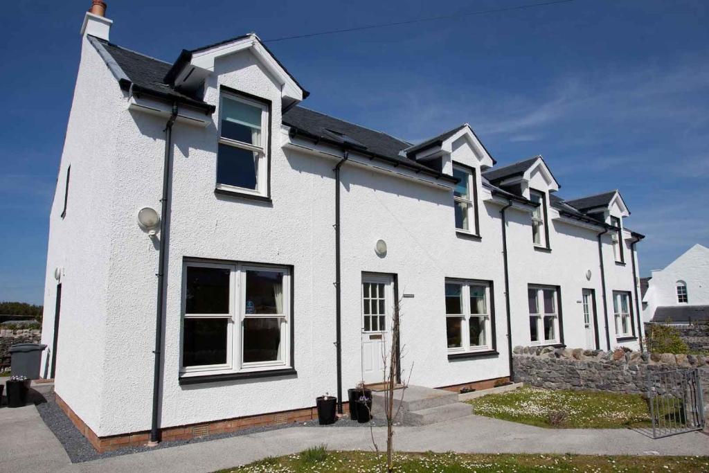 a white house with black windows and a stone wall at Killinallan Cottage in Port Charlotte