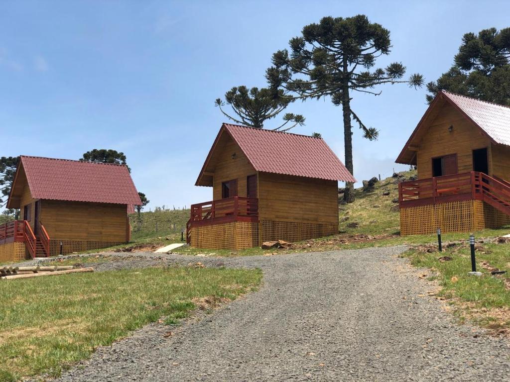 three wooden cottages on a hill with a dirt road at Pousada Bela Tereza in São Joaquim