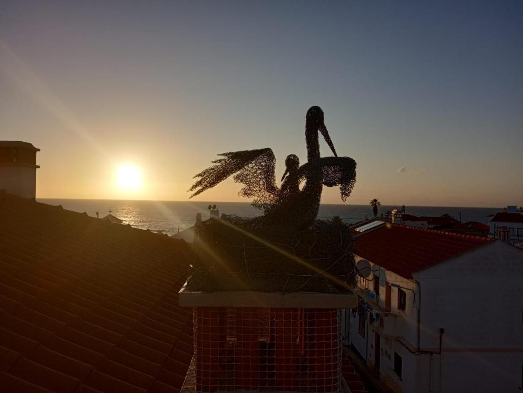 a statue on top of a building with the sunset in the background at Hostel Nature in Zambujeira do Mar