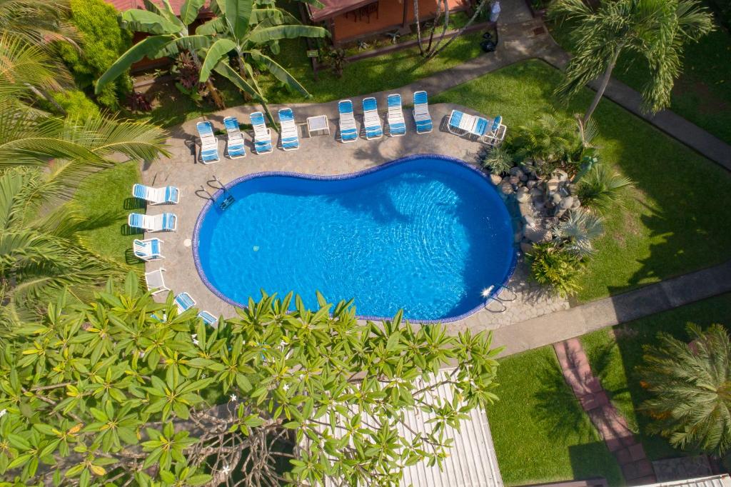 widok na basen z niebieskimi krzesłami i drzewami w obiekcie Hotel Los Ranchos w mieście Jacó