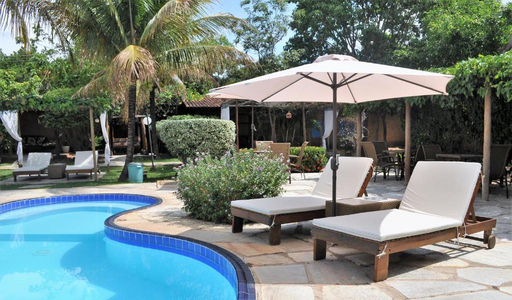 a pool with two lounge chairs and an umbrella at Pousada Flores do Cerrado in Pirenópolis