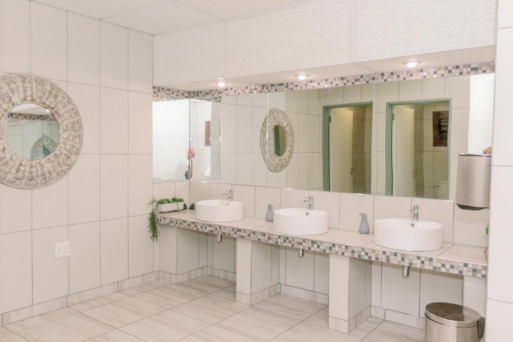 a bathroom with three sinks and two mirrors at Okahandja Country Hotel in Okahandja