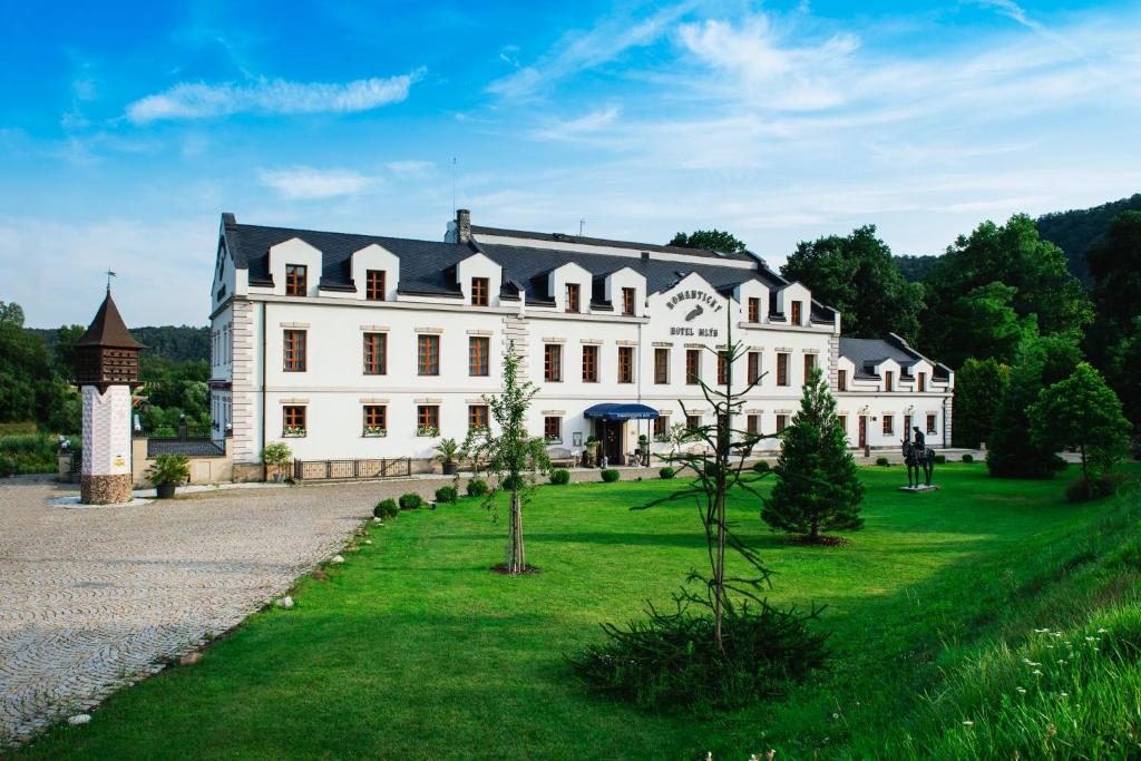 un grand bâtiment blanc avec un toit noir dans l'établissement Romantic Hotel Mlýn Karlstejn, à Karlštejn