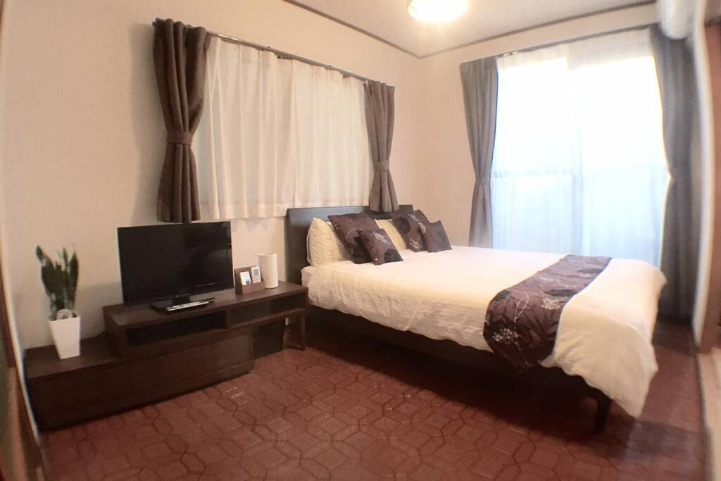 a bedroom with a bed and a tv and a window at 光アパートメント広島駅前 HIKARI Apartment Hiroshima Station in Hiroshima