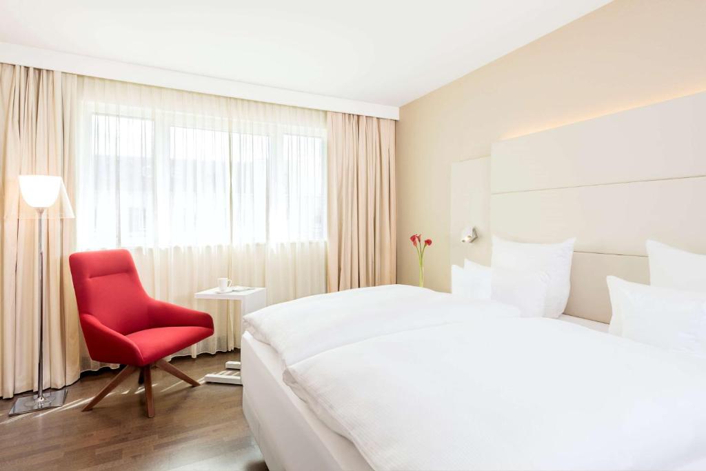 a bedroom with a large bed and a red chair at NH Collection Nürnberg City in Nuremberg