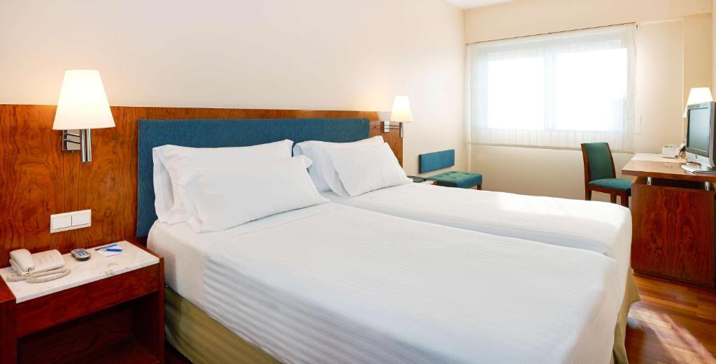 a hotel room with a large white bed and a telephone at NH Barcelona Entenza in Barcelona