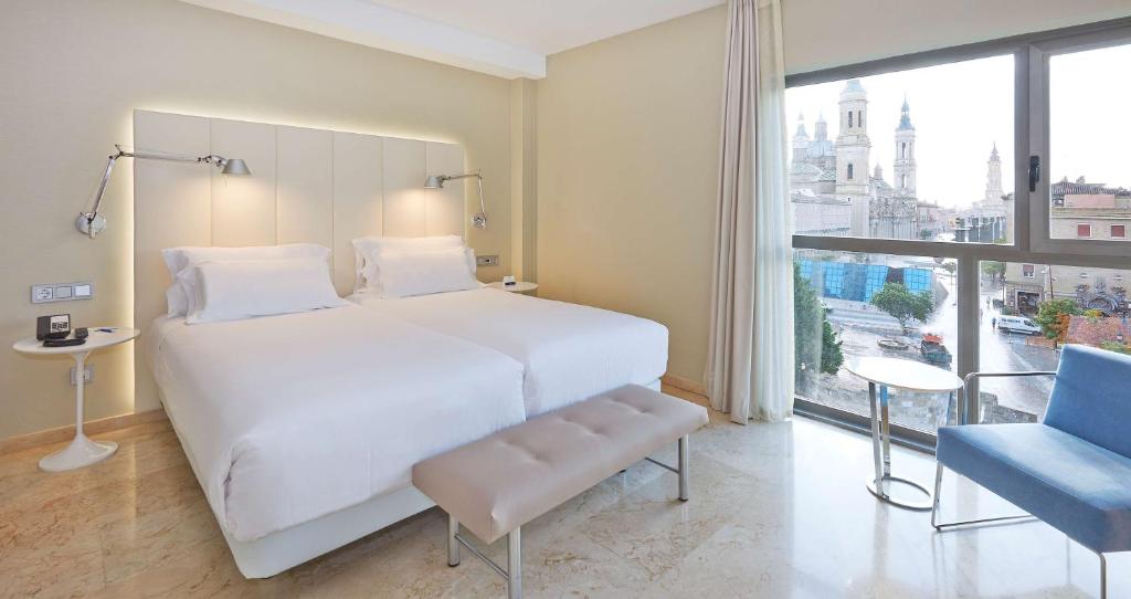 a bedroom with a white bed and a large window at NH Ciudad de Zaragoza in Zaragoza