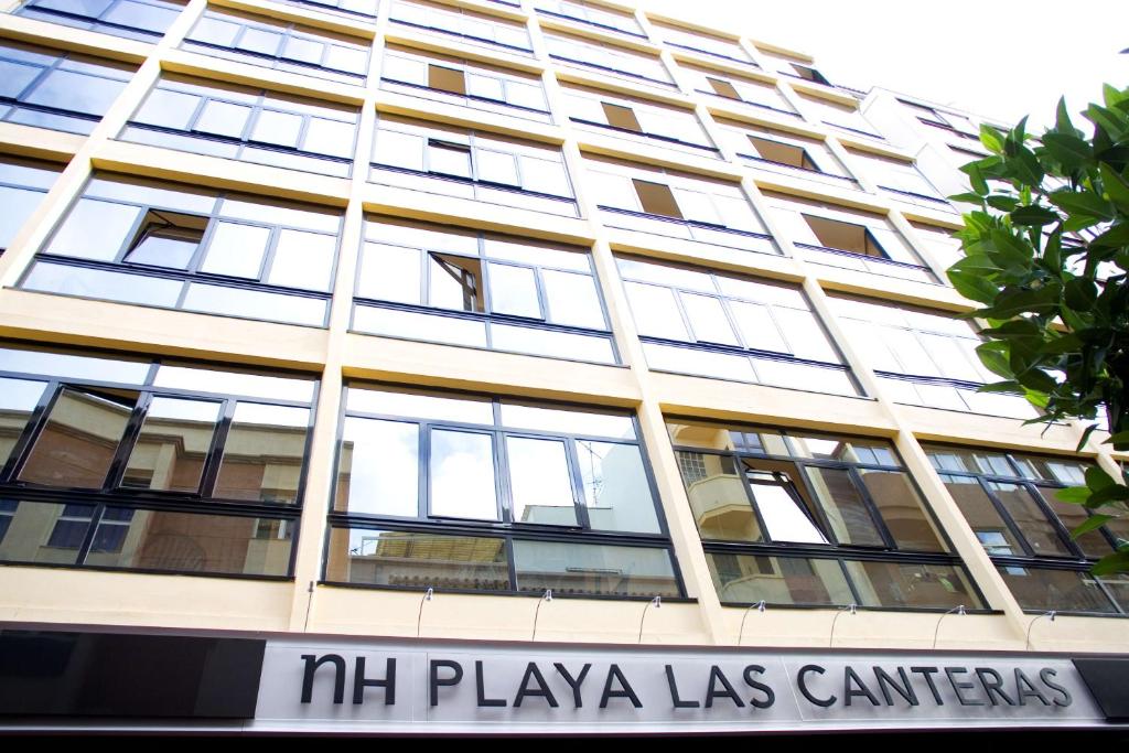 un grande edificio con un cartello di fronte di NH Las Palmas Playa las Canteras a Las Palmas de Gran Canaria