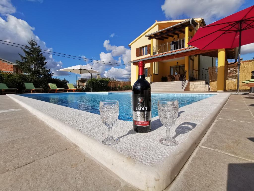a bottle of wine and two wine glasses next to a swimming pool at House ANA - Loborika, Pula, 4 bedrooms in Loborika