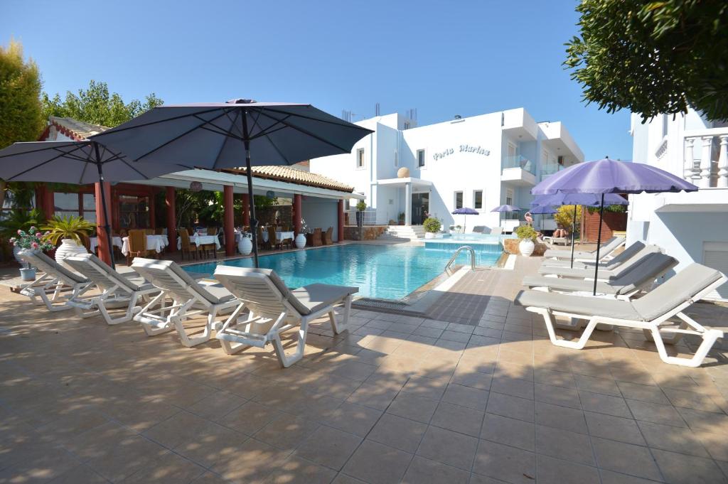 a group of chairs and umbrellas next to a pool at Perla Marina Aparthotel in Ialyssos