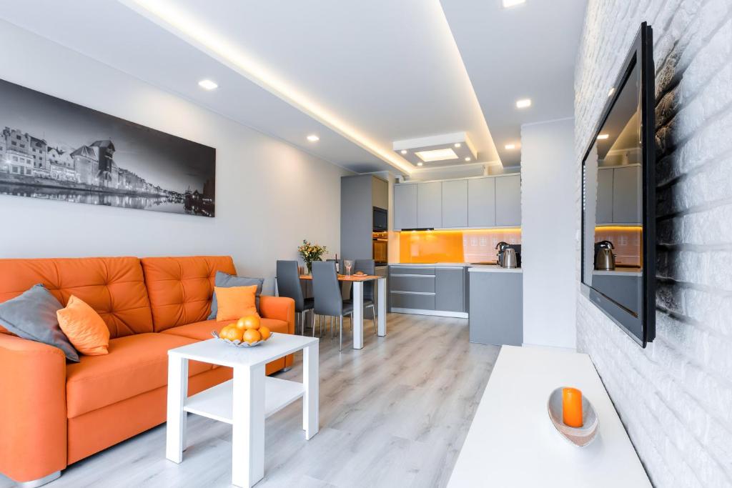 a living room with an orange couch and a kitchen at Apartment Orange Dream in Gdańsk