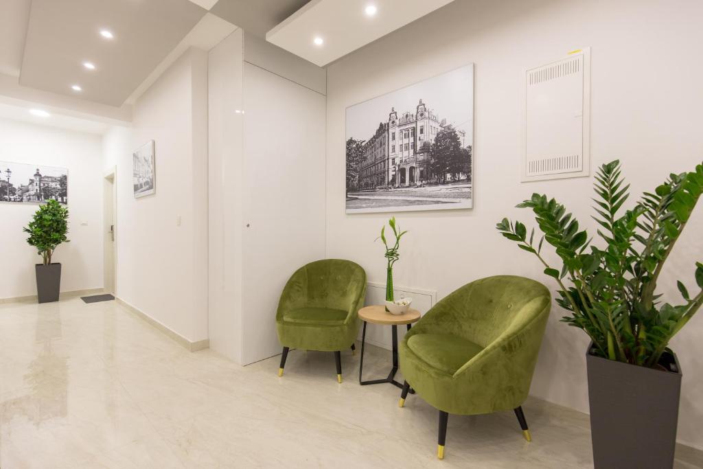 two green chairs and a table in a room with plants at Apartmani i sobe Pejačević in Osijek