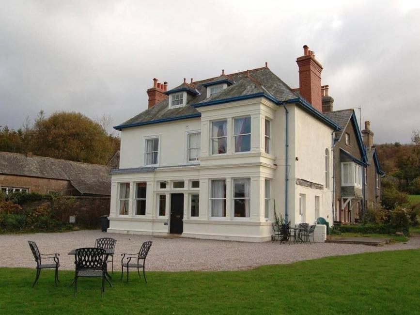 une grande maison blanche avec des chaises en face de celle-ci dans l'établissement Muncaster Cottages, à Ravenglass